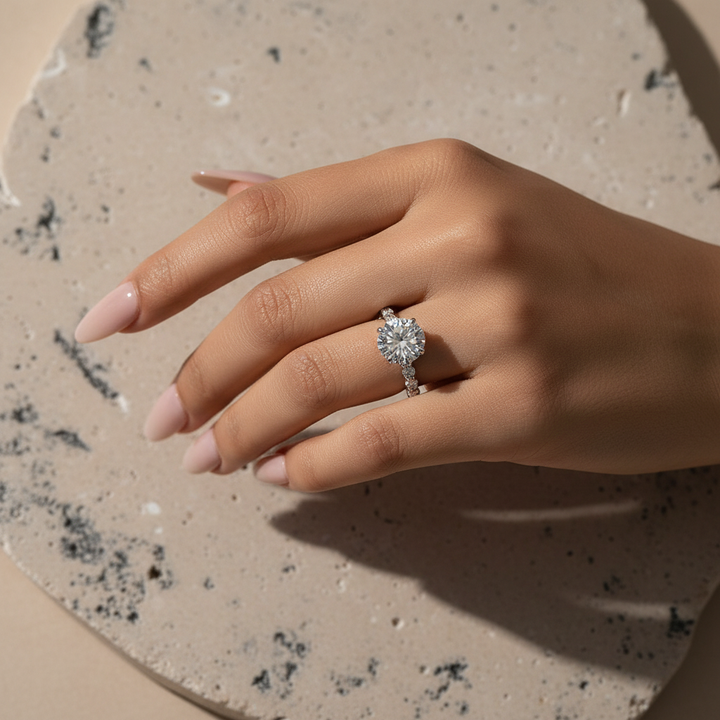 Round moissanite engagement ring worn on hand against a light textured background